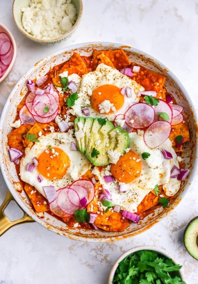Overhead view of red chilaquiles with egg and avocado in a pan.