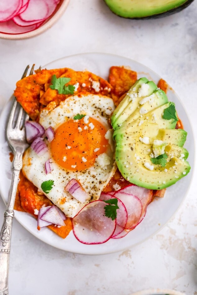 Red chilaquiles with an egg and avocado on a plate with a fork.