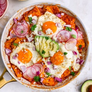 Eggs cooked in red chilaquiles topped with cotija cheese, avocado and radishes.