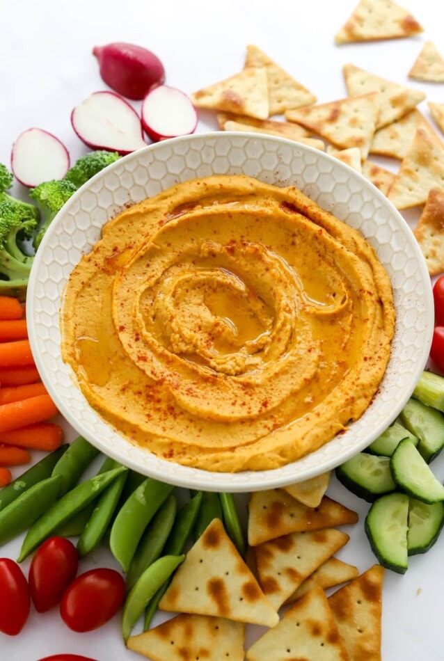 Sweet potato hummus in a serving bowl surrounded by veggies and pita for dipping.