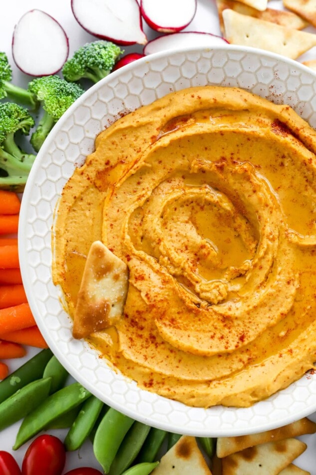 Close up of sweet potato hummus in a bowl. A pita chip rests in the hummus.