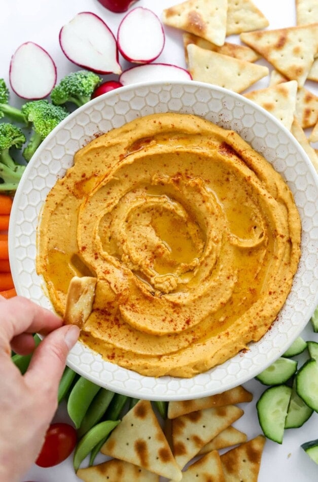 Dipping a pita chip into sweet potato hummus in a bowl.