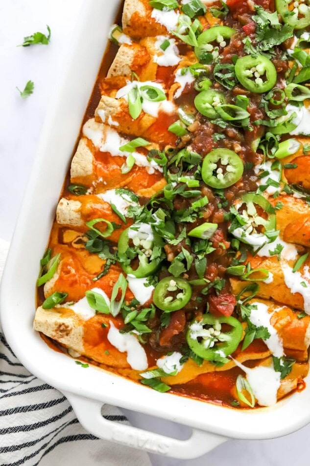 Overhead view of vegan enchiladas in a baking dish topped with green onions and jalapeños.