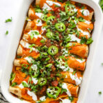 Vegan enchiladas in a baking dish topped with green onions and jalapeños.