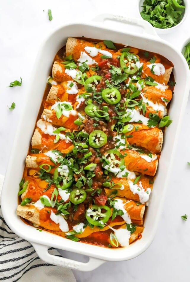 Vegan enchiladas in a baking dish topped with green onions and jalapeños.