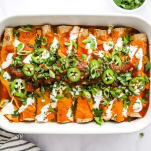Baked vegan enchiladas topped with green onion and jalapeño slices.