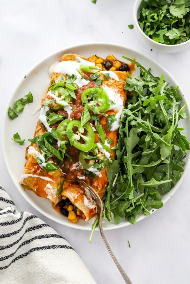 Two vegan enchiladas on a plate with salad greens.