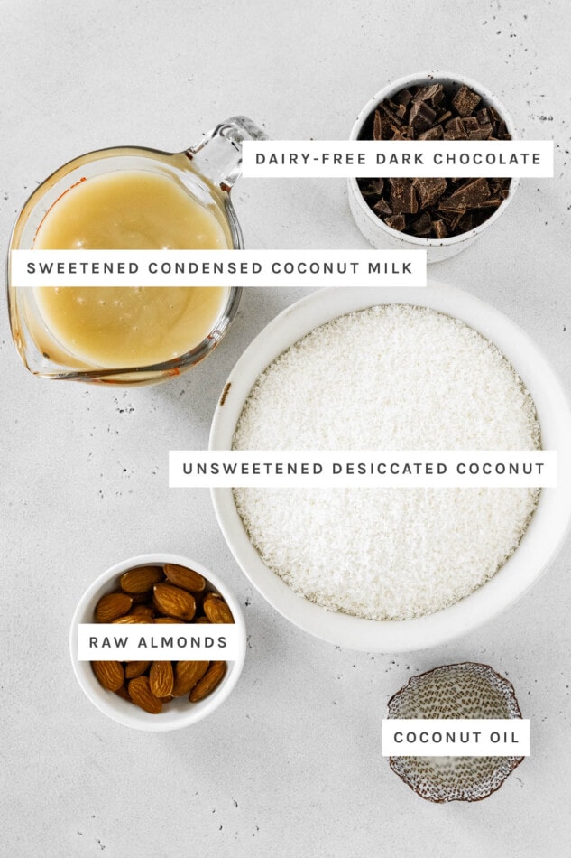 Ingredients measured out to make Healthy Almond Joy Bars: dairy-free dark chocolate, sweetened condensed coconut milk, unsweetened desiccated coconut, raw almonds and coconut oil.