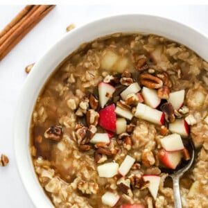 A bowl of apple cinnamon oatmeal topped with extra apple chunks and pecan pieces.