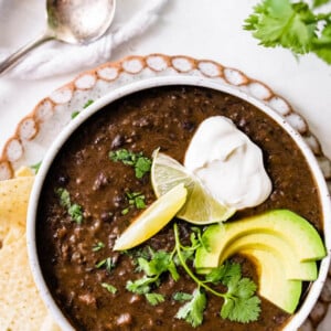 Bowl of black bean soup topped with cilantro, sour cream, lime and avocado. Tortilla chips are next to the bowl.