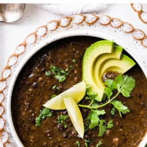 Bowl of black bean soup topped with cilantro, lime and avocado.