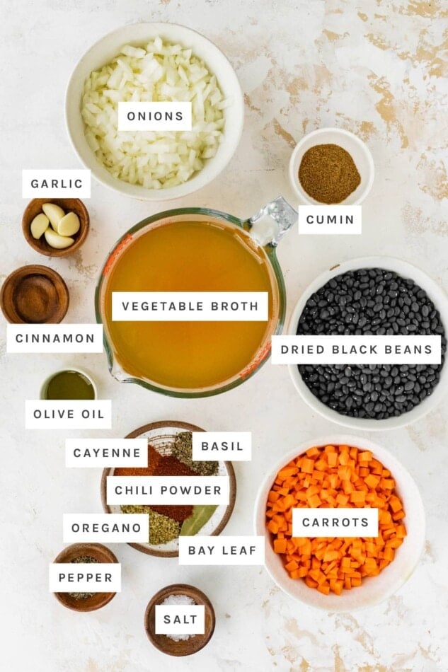 Ingredients measured out to make black bean soup: onions, cumin, garlic, vegetable broth, cinnamon, dried black beans, olive oil, cayenne, basil, chili powder, oregano, bay leaf, carrots, pepper and salt.