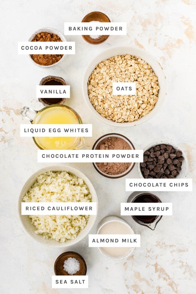 Ingredients measured out to make Cauliflower Brownie Baked Oatmeal: baking powder, cocoa powder, oats, vanilla, liquid egg whites, chocolate protein powder, chocolate chips, maple syrup, riced cauliflower, almond milk and sea salt.