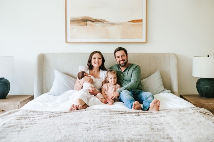 A family of four sitting on a bed.