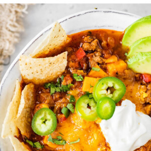 A bowl of no bean chili topped with cheese, jalapeños, avocado, sour cream and chips.