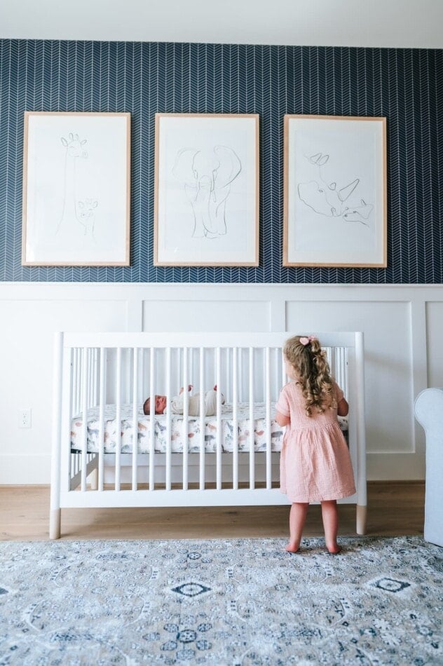 A big sister looking into a crib with newborn baby brother.