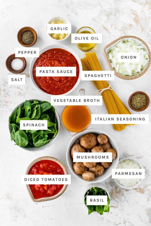 Ingredients measured out out to make one pot pasta: garlic, olive oil, onion, pepper, salt, pasta sauce, vegetable broth, spaghetti, spinach, Italian seasoning, mushrooms, diced tomatoes, parmesan and basil.