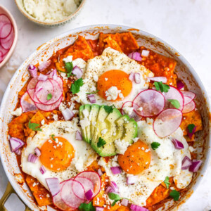 Overhead view of red chilaquiles with egg and avocado in a pan.