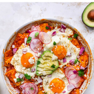 Overhead view of red chilaquiles with egg and avocado in a pan.