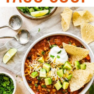 A bowl of taco soup topped with avocado chunks, shredded cheese and sour cream with tortilla chips.