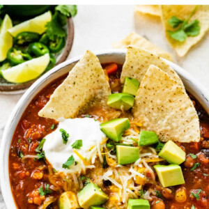 A bowl of taco soup topped with avocado chunks, shredded cheese and sour cream with tortilla chips.