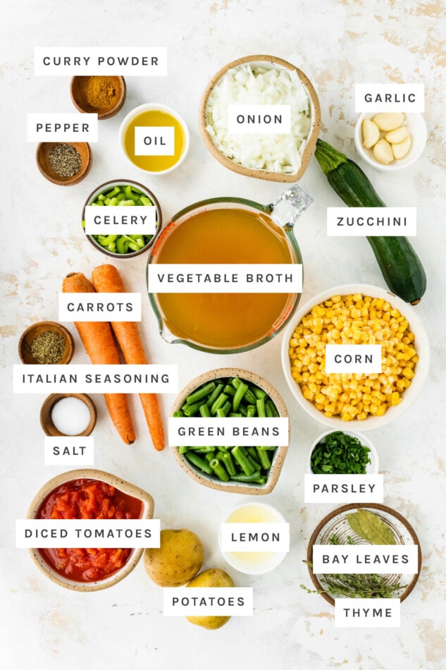 Ingredients measured out to make vegetable soup: curry powder, pepper, oil, onion, garlic, celery, vegetable broth, zucchini, carrots, Italian seasoning, corn, salt, green beans, parsley, diced tomatoes, potatoes, lemon, bay leaves and thyme.