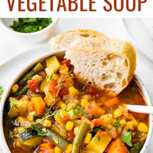 A bowl of vegetable soup with a chunk of bread dipped in the soup.