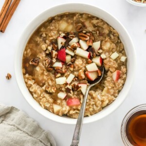 A bowl of apple cinnamon oatmeal topped with extra apple chunks and pecan pieces.