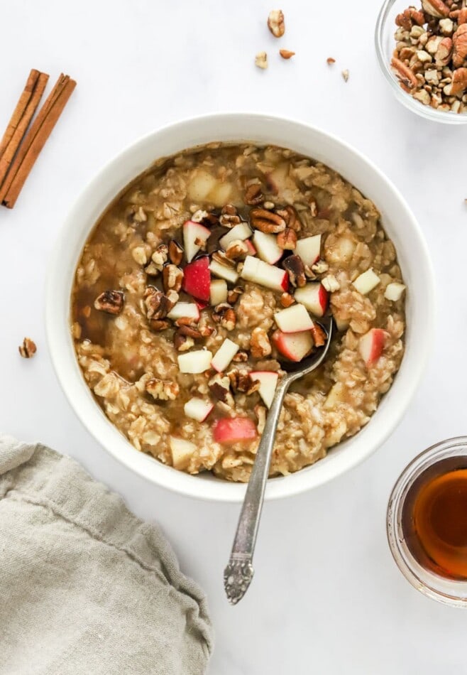 A bowl of apple cinnamon oatmeal topped with extra apple chunks and pecan pieces.