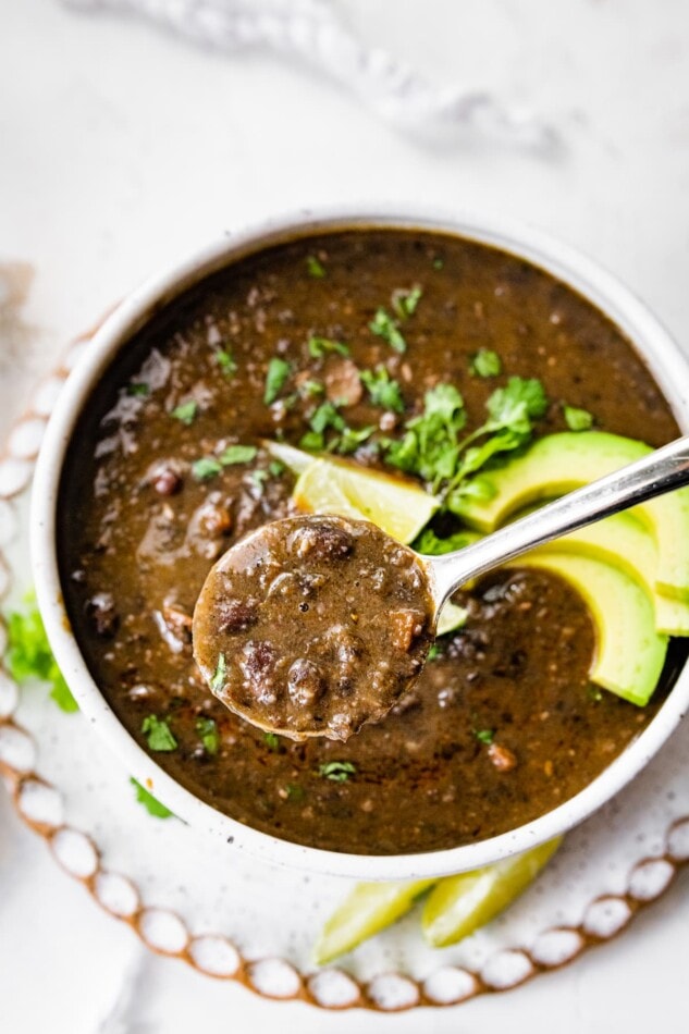 A spoonful of black bean soup lifted out of a bowl beneath it.