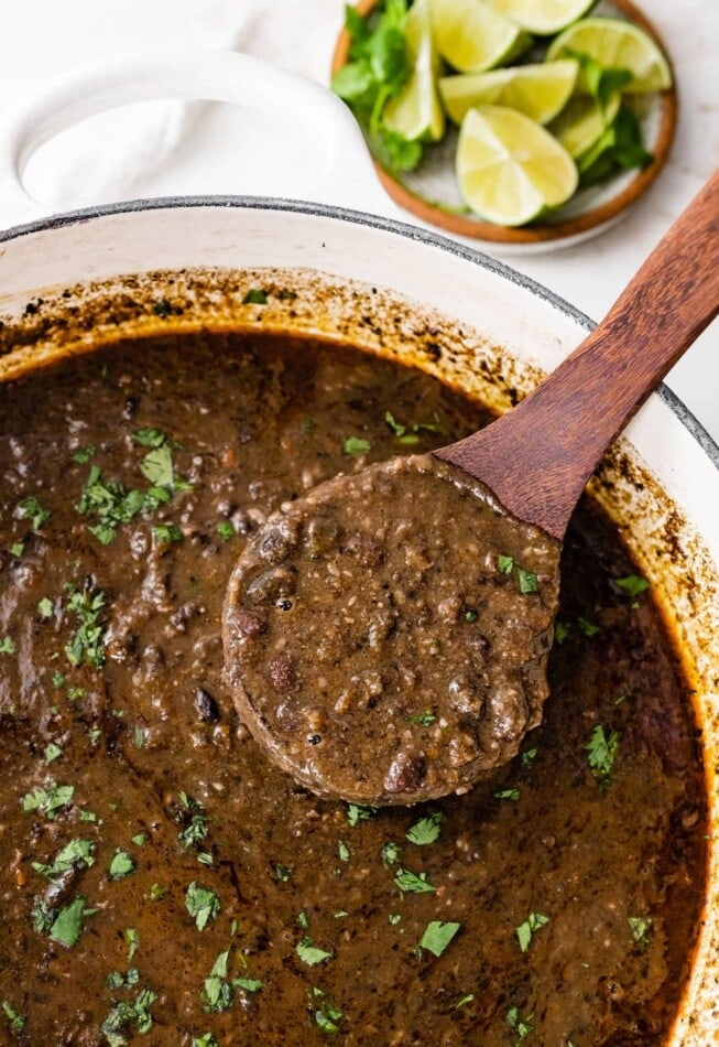 A wooden ladle with a portion of black bean soup over a pot beneath it.