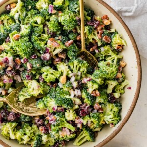 A serving bowl of broccoli cranberry salad with serving spoons.