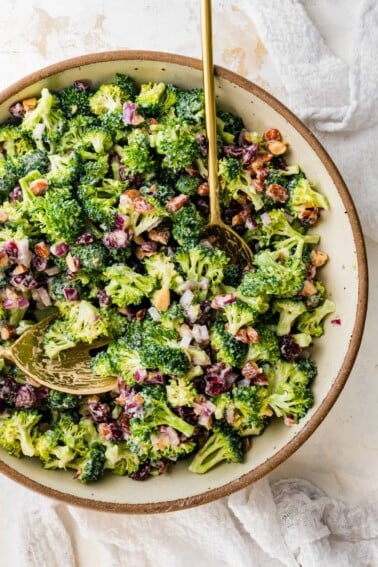 A serving bowl of broccoli cranberry salad with serving spoons.