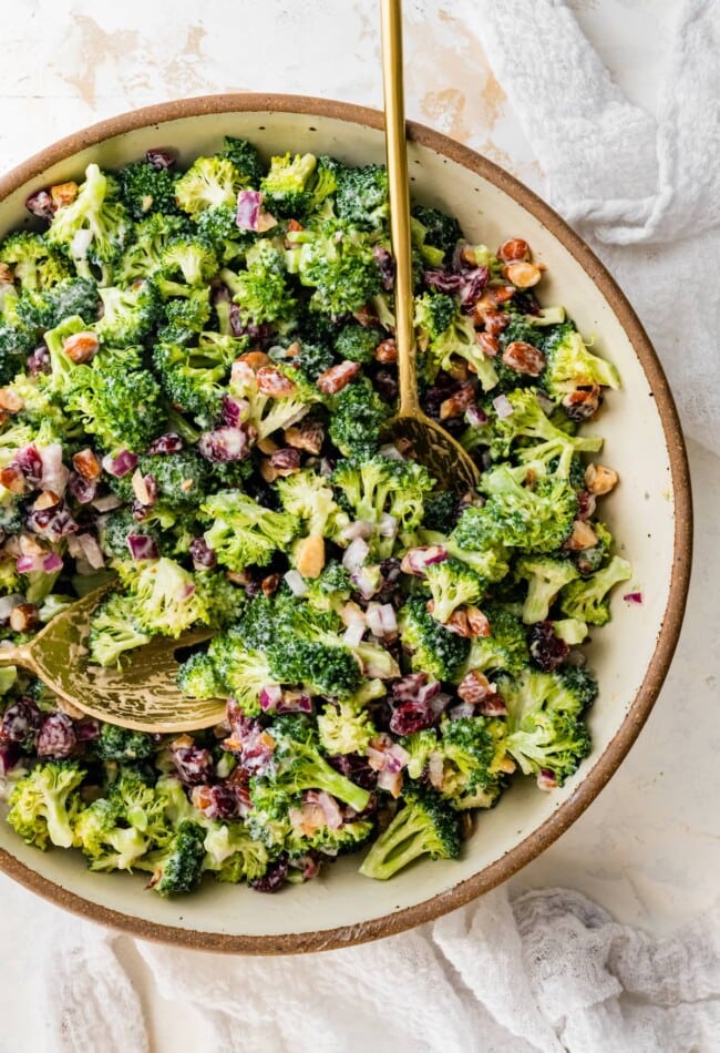 A serving bowl of broccoli cranberry salad with serving spoons.