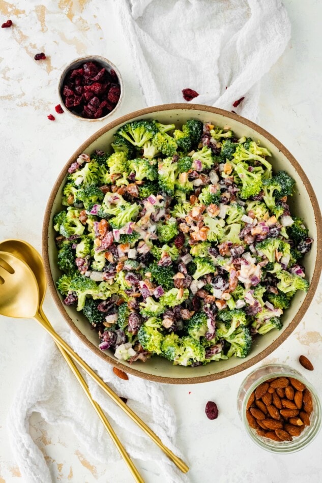 A serving bowl of broccoli cranberry salad with serving utensils to the side.