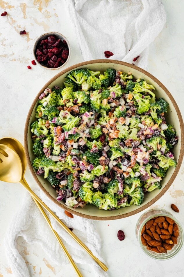 A serving bowl of broccoli cranberry salad with serving utensils to the side.