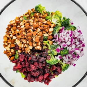 Broccoli, almonds, red onion and craisins in a glass mixing bowl.