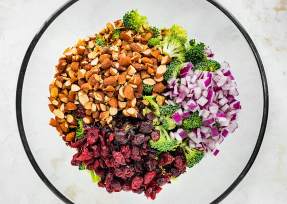 Broccoli, almonds, red onion and craisins in a glass mixing bowl.