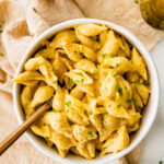 A bowl of vegan butternut squash mac and cheese topped with fresh pepper and chives. A fork rests in the bowl.