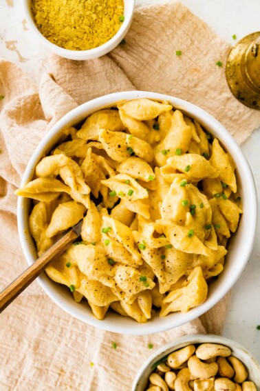 A bowl of vegan butternut squash mac and cheese topped with fresh pepper and chives. A fork rests in the bowl.