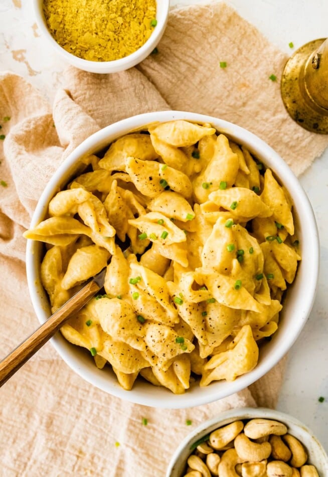 A bowl of vegan butternut squash mac and cheese topped with fresh pepper and chives. A fork rests in the bowl.