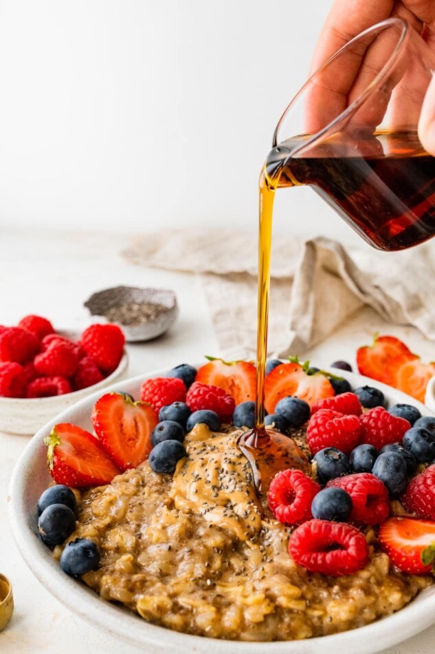 Pouring maple syrup onto a bowl of cauliflower oatmeal.