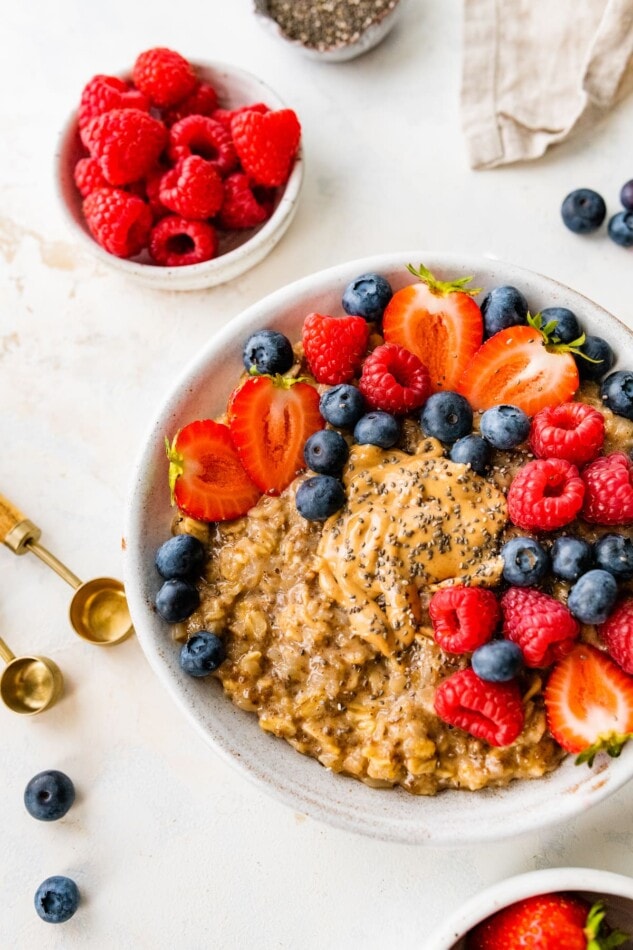 A bowl of cauliflower oatmeal topped with fresh mixed berries. A small bowl of raspberries in next to the bowl.