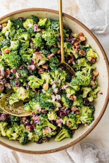 A serving bowl of broccoli cranberry salad with serving spoons.