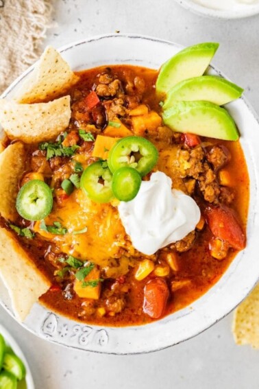 A bowl of no bean chili topped with cheese, jalapeños, avocado, sour cream and chips.