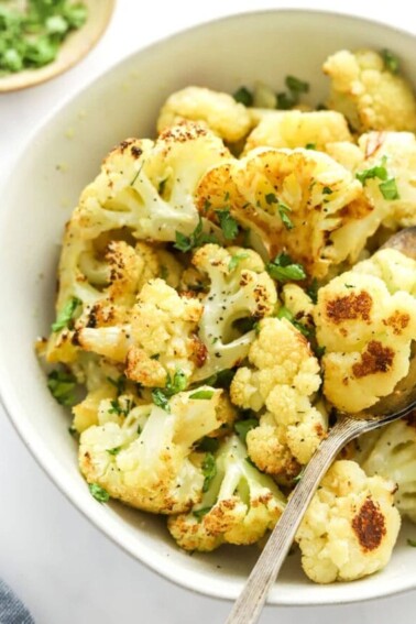 Close up of a bowl of roasted cauliflower. A serving spoon rests in the bowl.