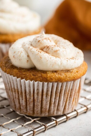 A frosted sweet potato muffin wrapped in a paper liner resting on a wire cooling rack.