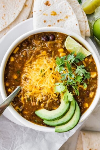 A bowl of vegetarian green chili served with shredded cheese, avocado, lime and cilantro.