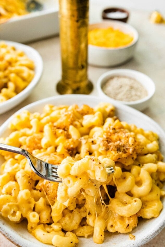A bowl of baked mac and cheese. A fork is removing a cheesy bite.