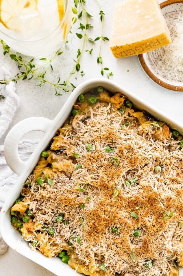 A baking dish containing healthy tuna noodle casserole next to a block of parmesan cheese.